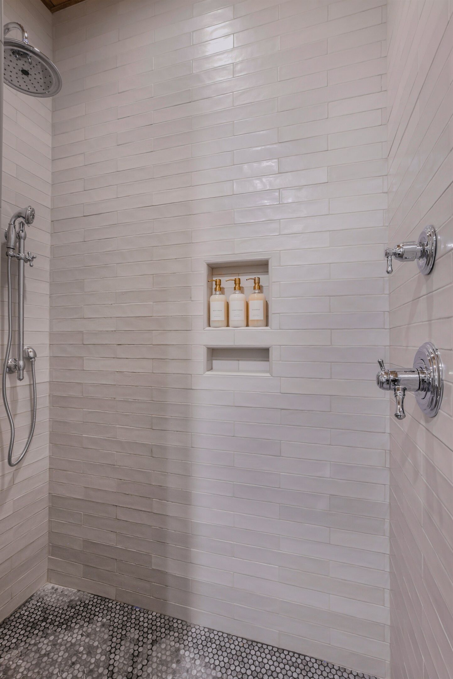 A shower with white tiled walls, a built-in shelf with toiletries, and a showerhead.