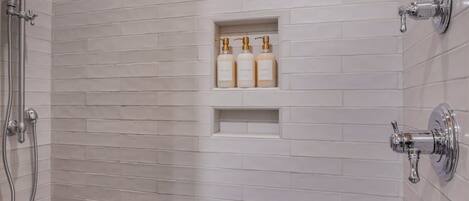 A shower with white tiled walls, a built-in shelf with toiletries, and a showerhead.