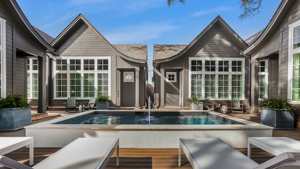 Uima-allas, jonka ympärillä on aurinkotuoleja ja ruukkukasveja. Allasta ympäröi puinen terassi ja rakennus, jossa on suuret ikkunat ja sälekaihtimet.