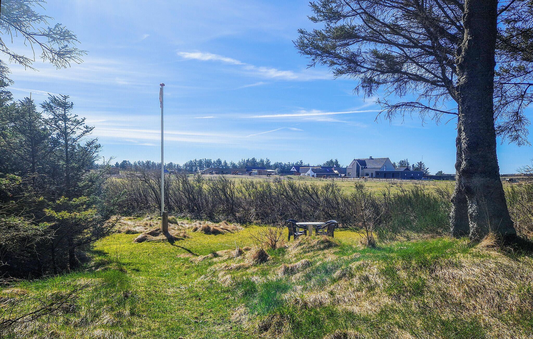 A rural landscape with a clear sky, a flagpole, and a building in the distance.