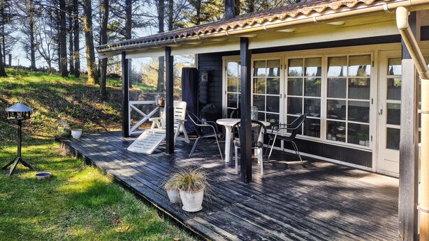 Un terrazzo in legno con sedute all'aperto, un pergolato e vista sulla foresta circostante.
