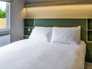 Una cama con ropa blanca en una habitación con cabecera verde y estanterías empotradas.