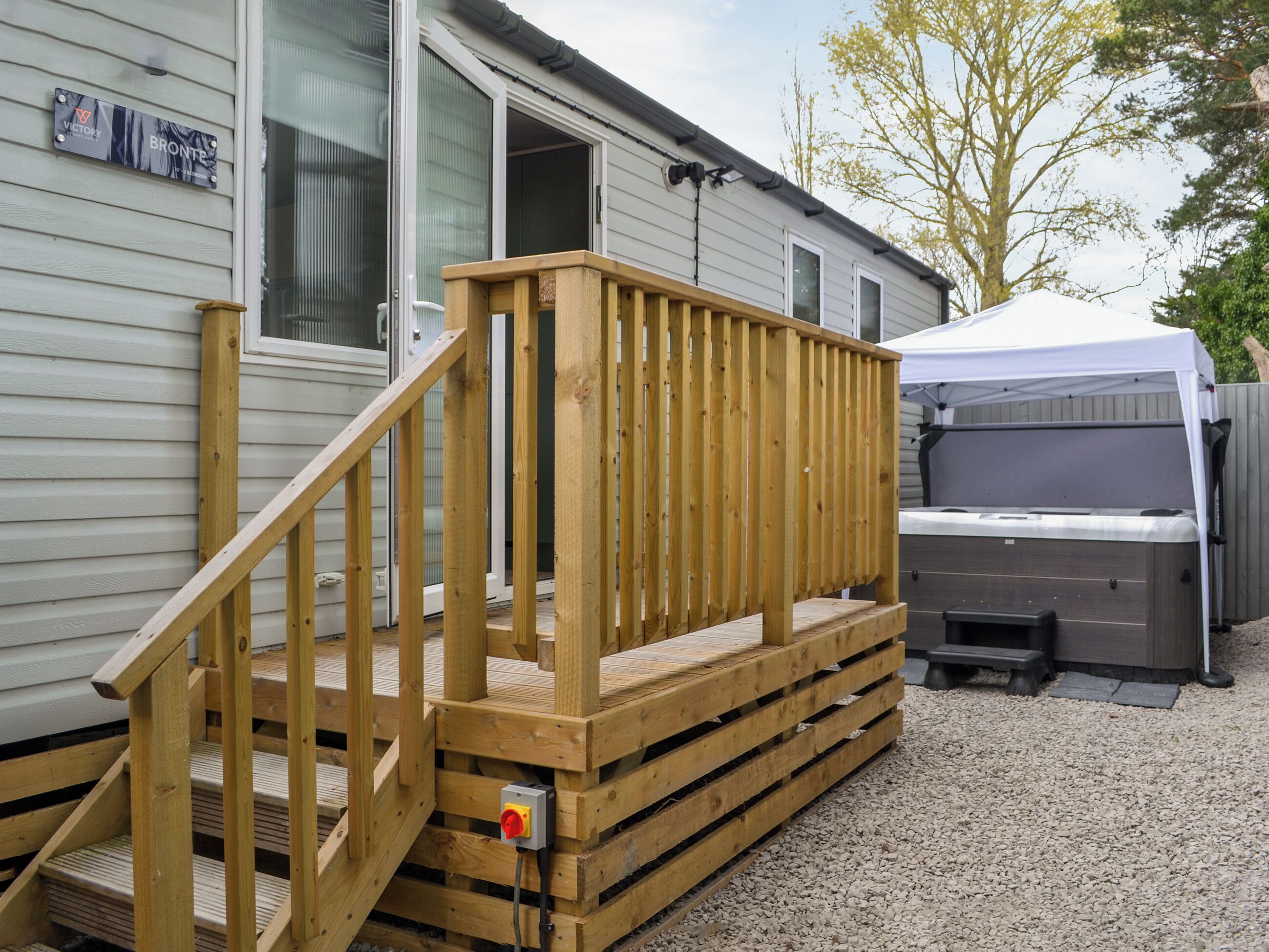 A wooden deck with a ramp leading to a covered patio area, a hot tub, and a grill.