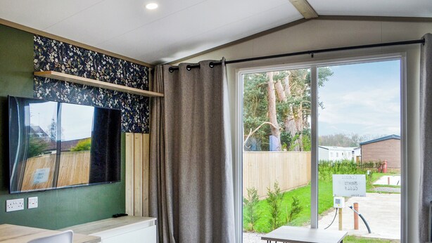 Ein modernes Zimmer mit großem Fenster, Flachbildfernseher, kleinem Tisch und einer Couch.