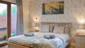 A bedroom with a large bed, two bedside tables with lamps, a painting on the wall, and a view through a sliding door. - A great location to explore the stunning East Riding of Yorkshire. (Fitling)