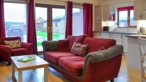 A cozy living room with a red sofa, a small table, and a view of a car outside through large windows. - A great location to explore the stunning East Riding of Yorkshire. (Fitling)