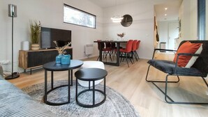 Ein modernes Wohnzimmer mit einer Couch, einem Couchtisch, einem Esstisch mit Stühlen, einem Fernseher und einer Wanduhr.