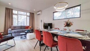 Ein modernes Wohnzimmer mit einer Couch, einem Esstisch für vier Personen und einem Fernseher.