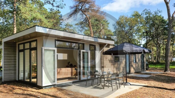Eine moderne, kompakte Hütte mit Glastür, einer Terrasse und Gartenmöbeln sowie einem großen Sonnenschirm.