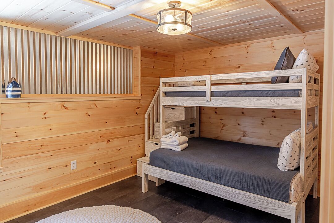A wooden cabin room with a bunk bed, a small table, and a ceiling light.