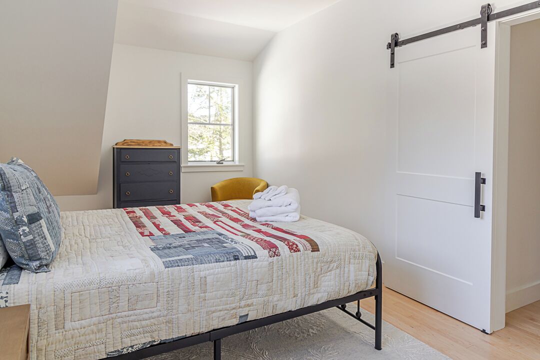 Une chambre à coucher comprenant un lit, une commode, une chaise et une porte coulissante.