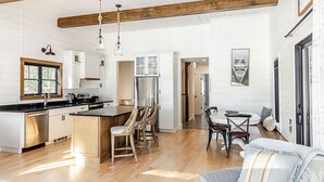 A spacious kitchen with wooden beams, a central island, and a dining area with a table and chairs. - Lakefront, brand new, craftsman style 4-bedroom 2 bath house home on Long Lake. (Bridgton)