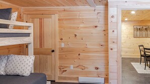 A cozy cabin interior with a bunk bed, a wooden wall, and a dining area. - Lakefront, brand new, craftsman style 4-bedroom 2 bath house home on Long Lake. (Bridgton)