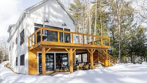 A two-story wooden house with a balcony, surrounded by snow and trees. - Lakefront, brand new, craftsman style 4-bedroom 2 bath house home on Long Lake. (Bridgton)