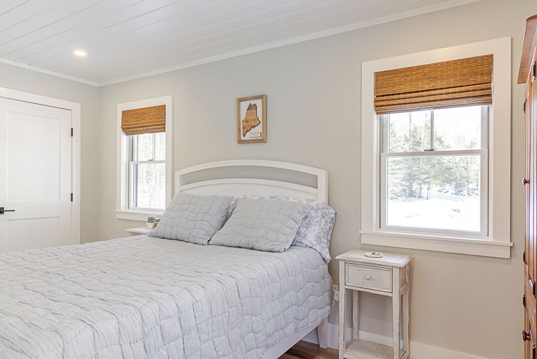 A bedroom with a bed, two bedside tables, and two windows with blinds.