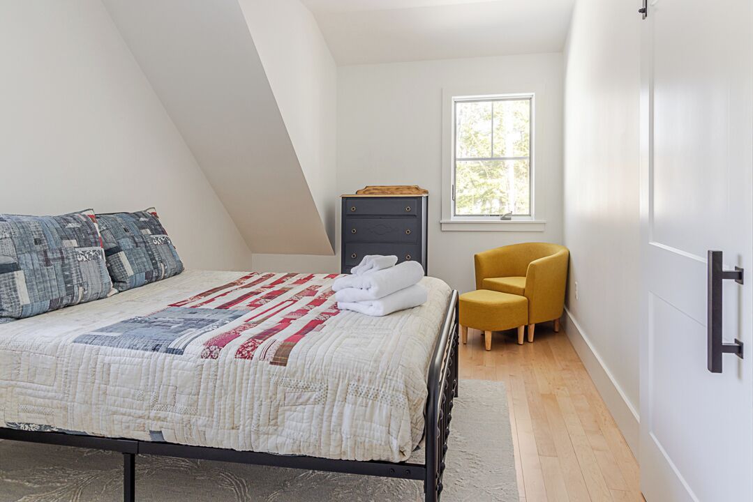 A bedroom with a bed, a window, a chair, and a wardrobe.