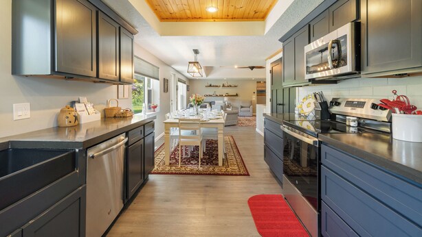 A modern kitchen with dark cabinets, stainless steel appliances, and a wooden ceiling.
