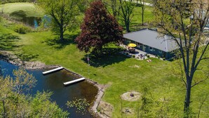 An aerial view of a house with a pond, a dock, and a patio area with outdoor furniture.