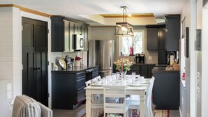 A modern kitchen with dark cabinetry, a central island, and a dining area with white chairs and a table set for four.