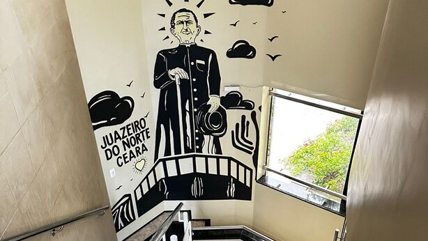 Una escalera con un mural que muestra a un hombre sosteniendo un sombrero y una maleta, rodeado de nubes y pájaros.