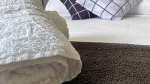 Una cama bien hecha con una manta blanca y dos almohadas, una con estampado de cuadros.