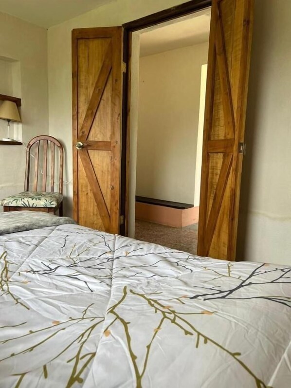A bedroom with a bed, a wooden door, and a chair. - Bhoga Forest Orosi (Agua Caliente)