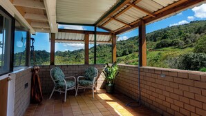 A covered patio with two chairs and a potted plant, overlooking a lush green landscape.