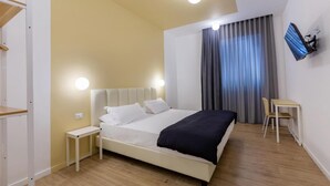 Un dormitori modern amb llit, taules de nit, escriptori i televisió penjada a la paret.