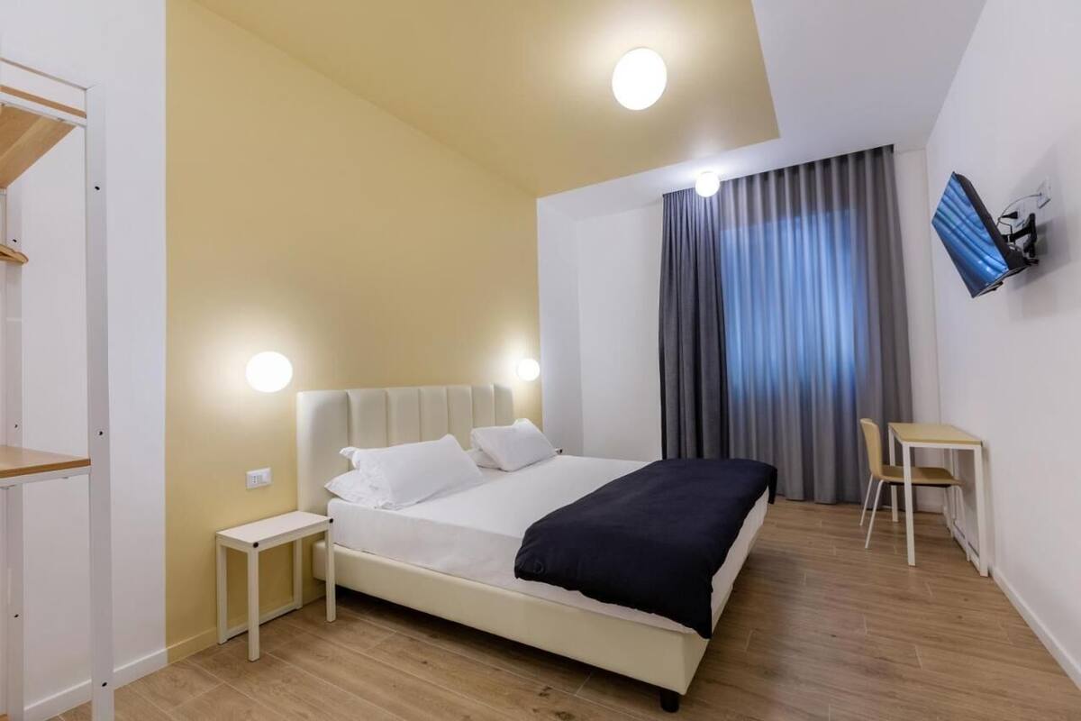 A modern bedroom with a bed, bedside tables, a desk, and a TV mounted on the wall.