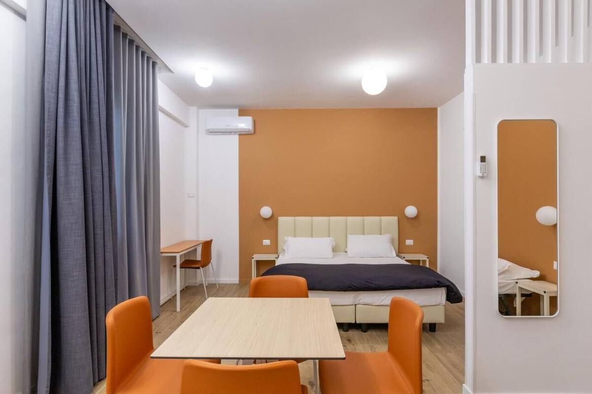 A hotel room with a bed, a table, two chairs, a desk, and a mirror.