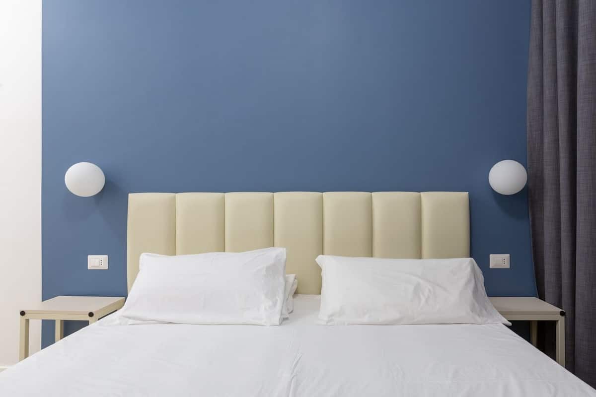 A bed with a beige upholstered headboard, white pillows, and a blue wall.