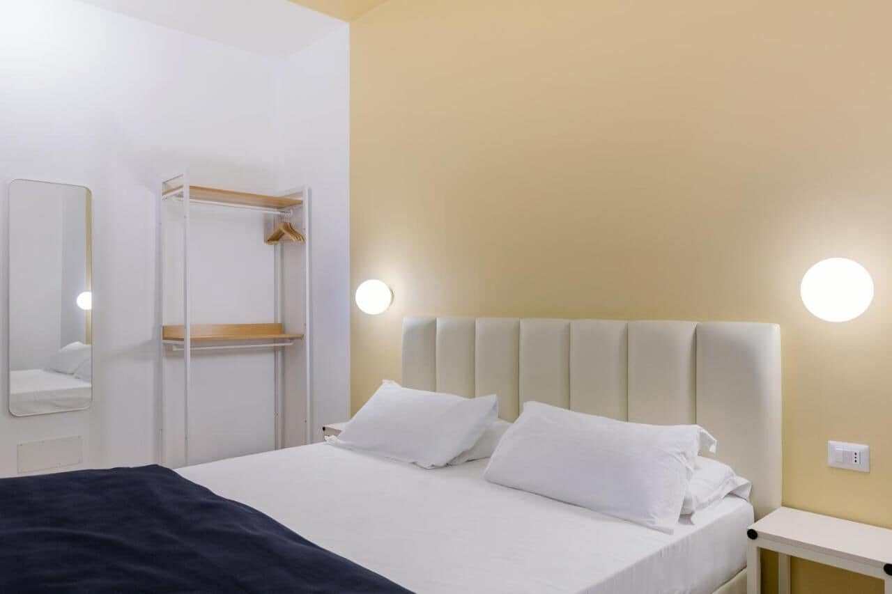 A hotel room with a bed, a bedside table, a nightstand, a mirror, and a wardrobe.