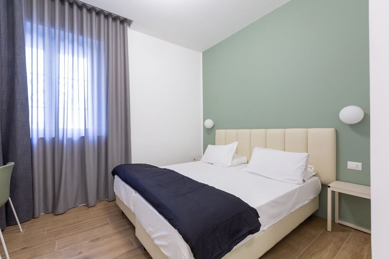 A bedroom with a bed, a chair, a bedside table, and a window with curtains.