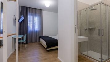 A small, modern room with a bed, a desk, and a shower area.