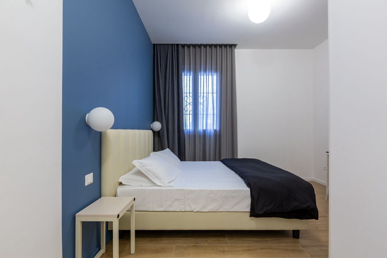 A bedroom with a bed, a bedside table, and a window with curtains.
