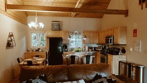 Un salon chaleureux avec un canapé en cuir et un coin repas doté de meubles en bois. On aperçoit, au fond, une cuisine avec des armoires en bois et des appareils modernes.