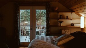 Une pièce chaleureuse avec un plafond en bois, un lit recouvert d’une literie à motifs, une petite table et une fenêtre donnant sur une terrasse.