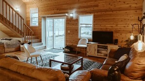 L’intérieur d’un chalet confortable, avec un escalier, un téléviseur et une cheminée.