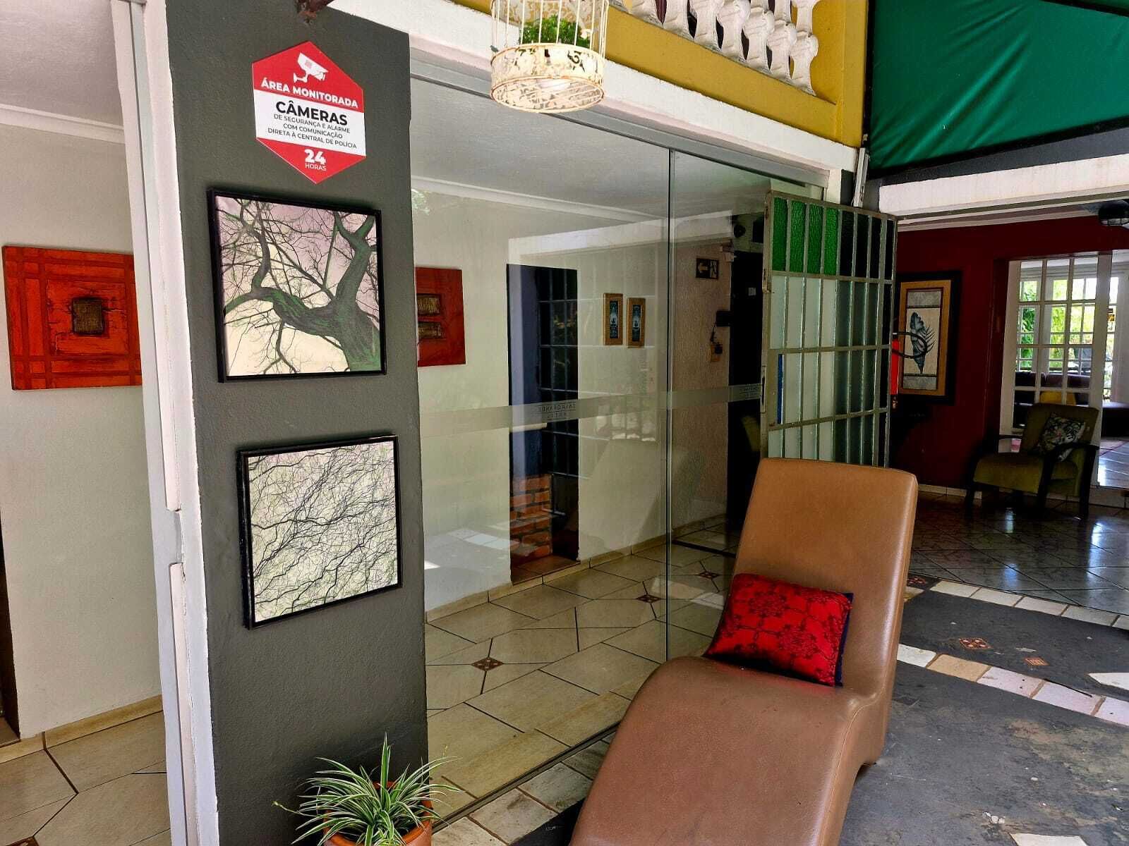 Un hall d’entrée avec un mur en verre, un fauteuil en cuir marron agrémenté d’un coussin rouge et un panneau indiquant la présence d’une caméra de surveillance.