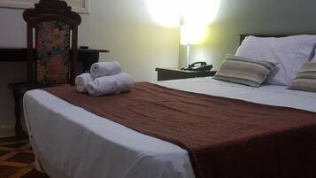 Habitación de hotel con cama, mesita de noche, lámpara y ventana con persianas.