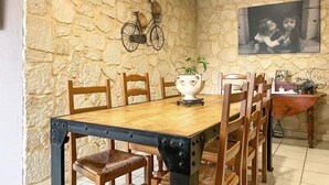 A dining area with a stone wall, wooden chairs, a wooden table, a decorative vase, and a framed photo on the wall. - Nice home in Montfrin (Montfrin)