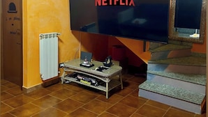 A living room with a large flat-screen TV mounted on the wall, a staircase with a mirror, and a radiator on the floor.