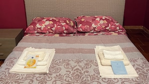 A neatly made bed with floral pillows, a decorative wall with 'Mr' and 'Mrs' signs, and a bedside table with a tissue box and a small item.