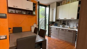 A compact kitchen with white cabinets, a dining table with chairs, and a view of greenery outside.