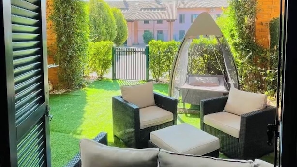 An outdoor seating area with wicker furniture and cushions, a green lawn, and a view of a residential building in the background.