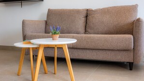 Ein braunes Sofa mit Holzbeinen, ein weißer runder Tisch mit einer Pflanze und ein kleines Regal mit einem Buch.