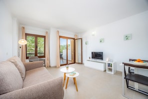 Ein modernes Wohnzimmer mit einer Couch, einem kleinen Tisch, einem Fernseher und einem Balkon mit Vorhängen.