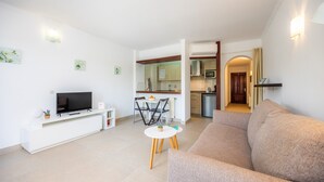 Ein modernes Wohnzimmer mit Flachbildfernseher, einer Couch, einem kleinen runden Tisch und einer Essecke mit Stühlen.