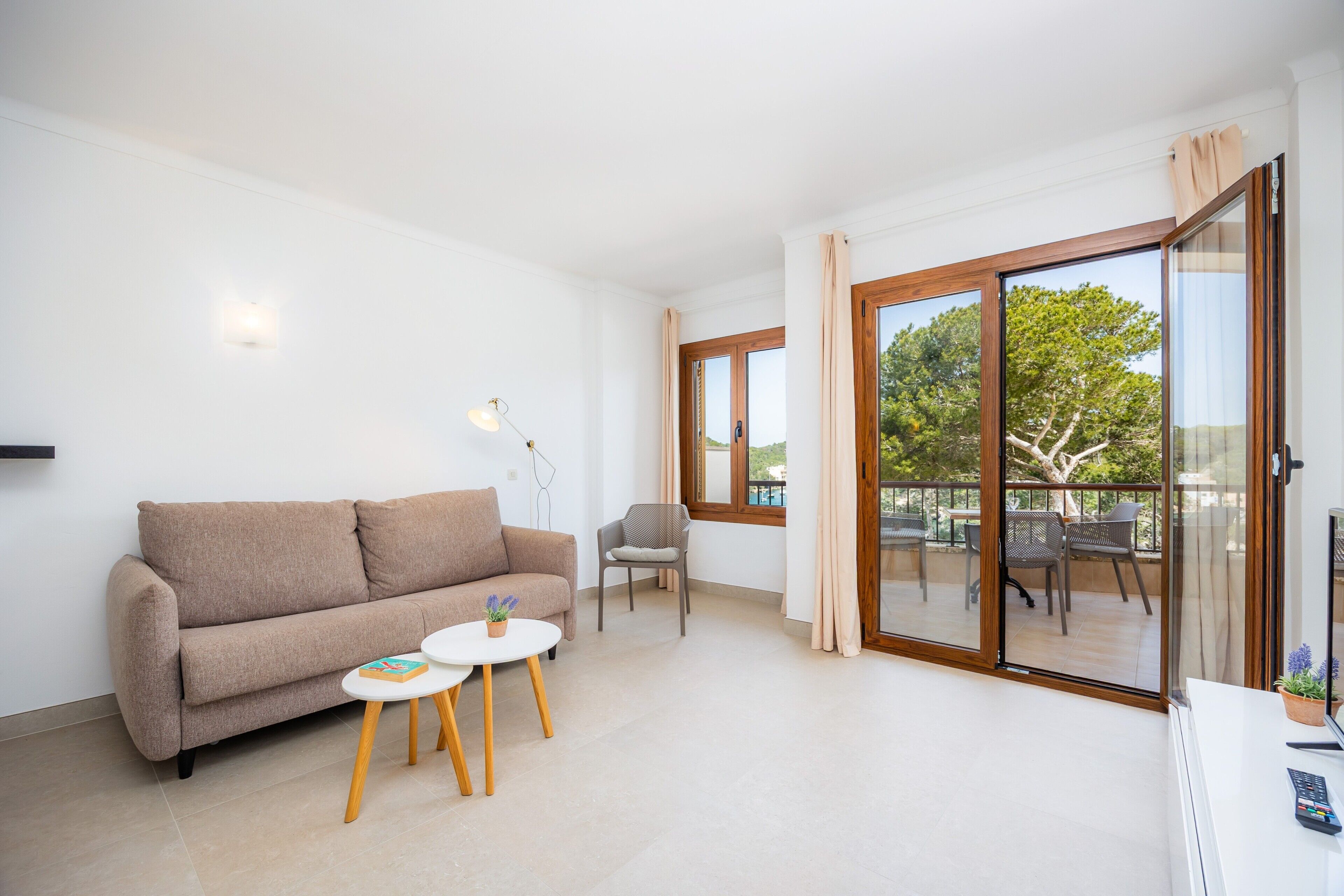 Un salon comprenant un canapé, deux petites tables, un fauteuil et une porte-fenêtre coulissante donnant sur un espace extérieur avec une table et des chaises.