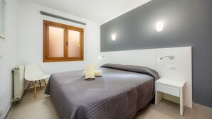 Un dormitorio con cama, mesita de noche, silla y ventana.